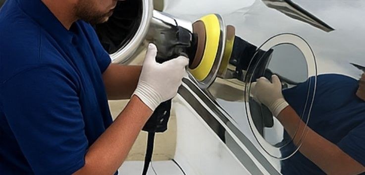 Technician machine-polishing a business jet fuselage during aircraft detailing